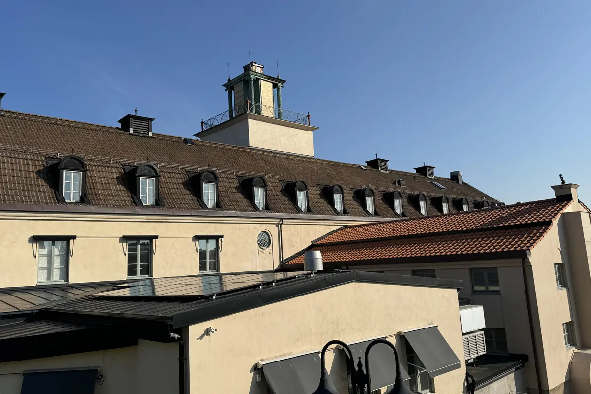 Hög byggnad med putsad fasad och ett torn. Ovanpå taket på en utbyggnad skymtar solcellspaneler. 
