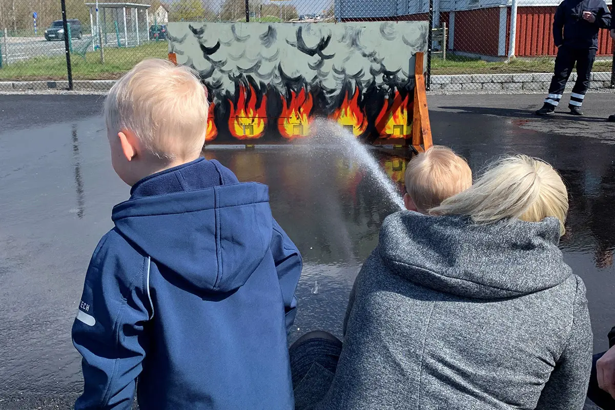 Barn sprutar vatten mot ett plank med eldsflammor. 