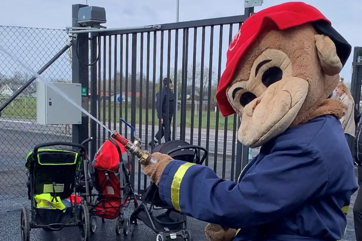 Räddningstjänstens maskot Flammy, en apa med röd mössa och brandmanskläder. Flammy sprutar vatten med slang på bilden.