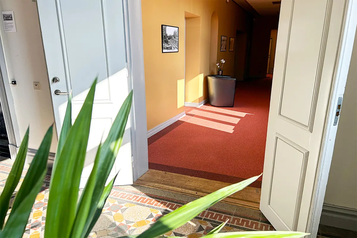 Pardörrar öppna mot en korridor. Gula väggar och rött golv. 