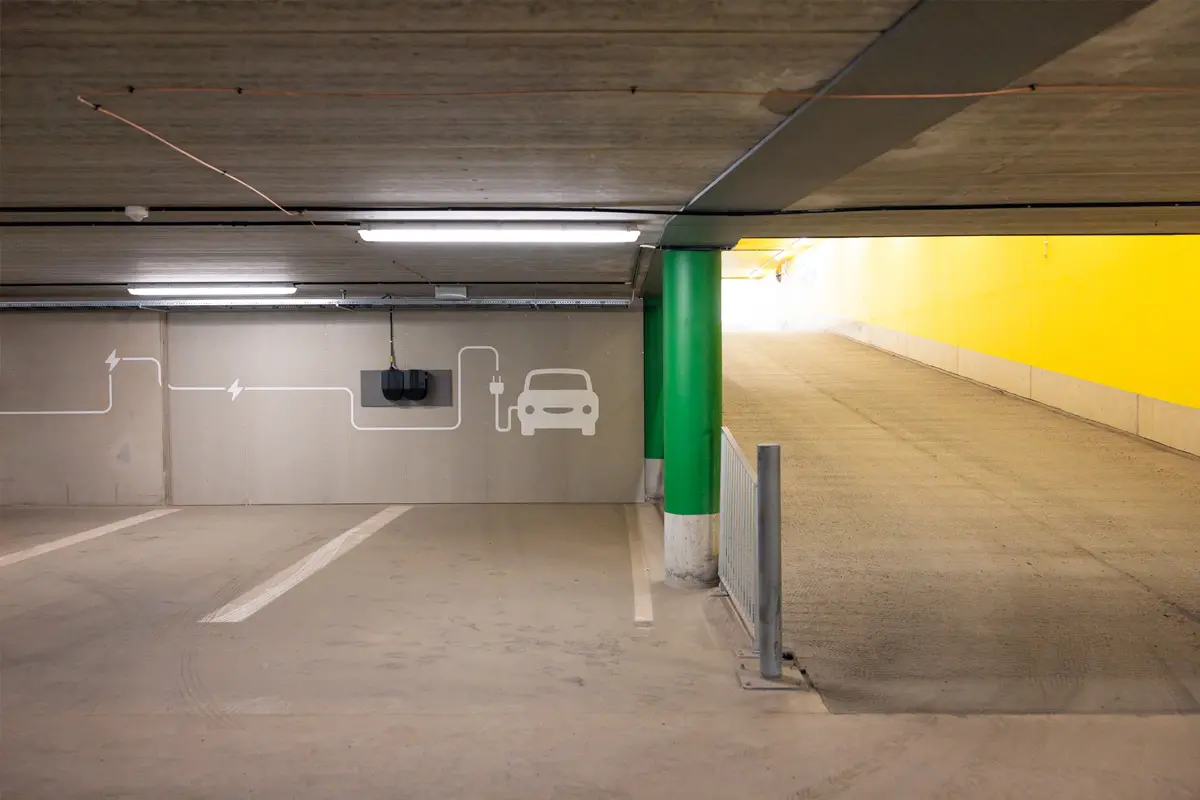 Laddplaser i parkeringsgarage. På betongväggen är en glad bil målad, laddsladden löper i mönster längs väggen.