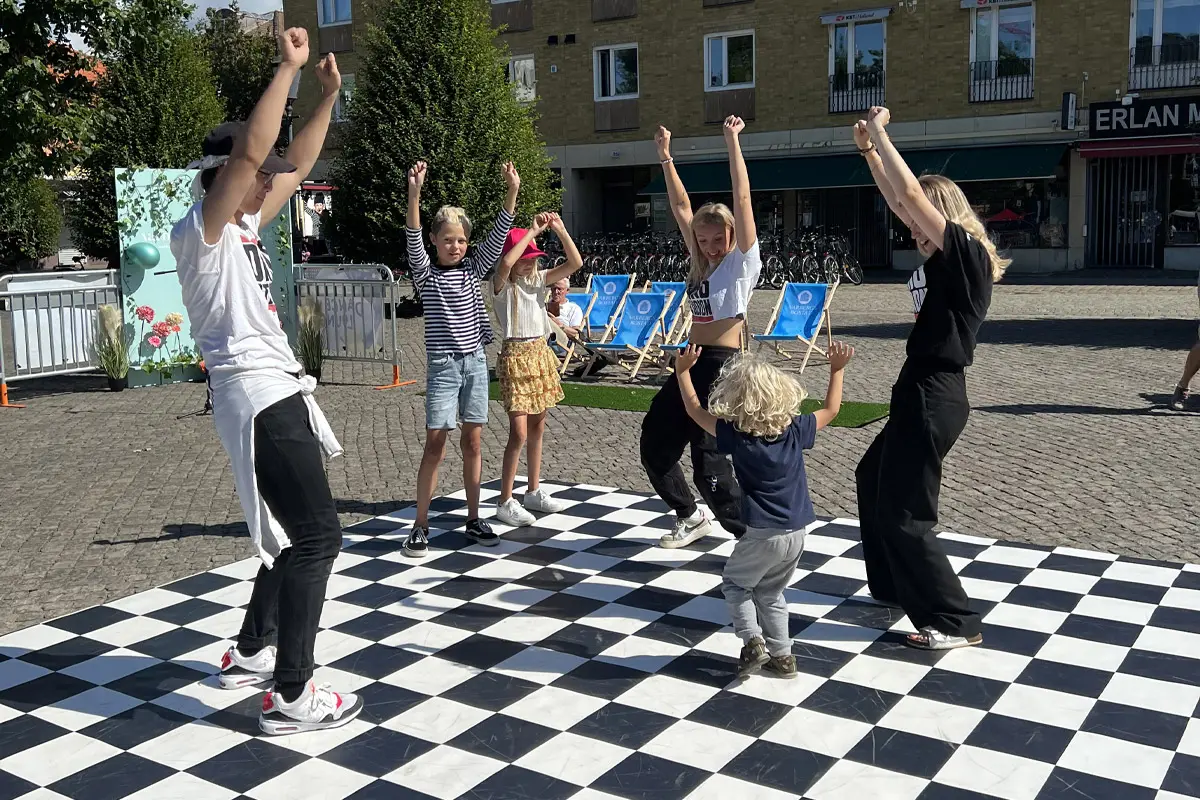 En grupp barn och tonåringar dansar på en schackrutig matta på Varbergs torg.